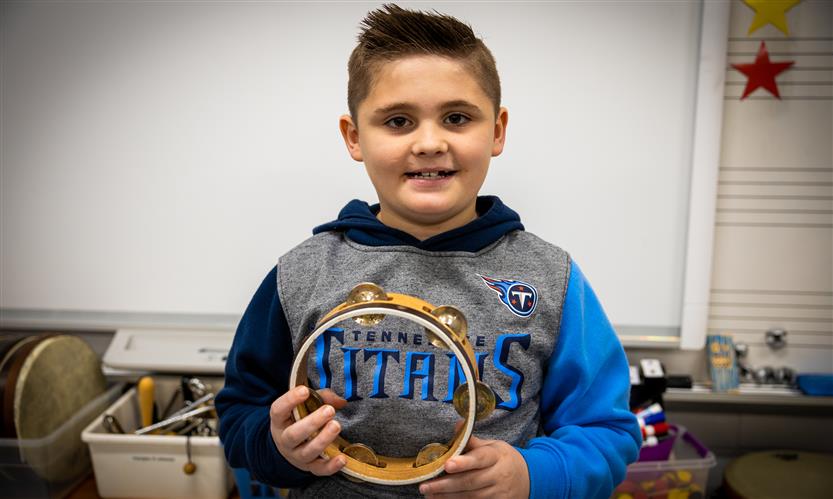 A boy smiles while holding an instrument